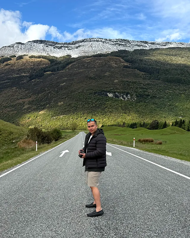 Sherwin with his camera on a road below snow-capped mountains in New Zealand